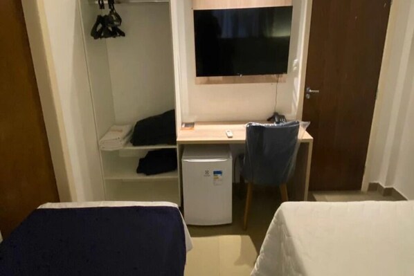 A room with a bed, a desk with a computer, a TV, and a small refrigerator. - Hotel Bastos (Euclides Da Cunha)