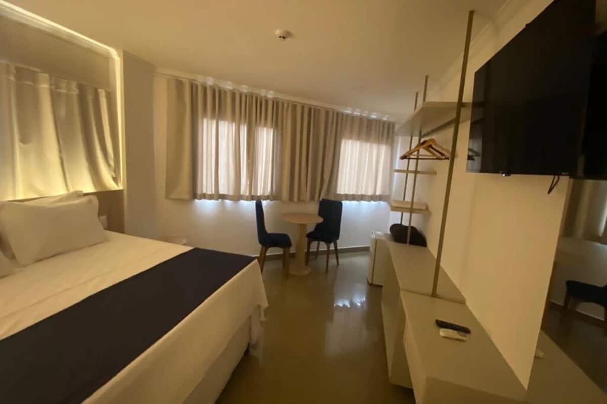 A hotel room with a bed, a desk, a chair, a TV, and a window with curtains.