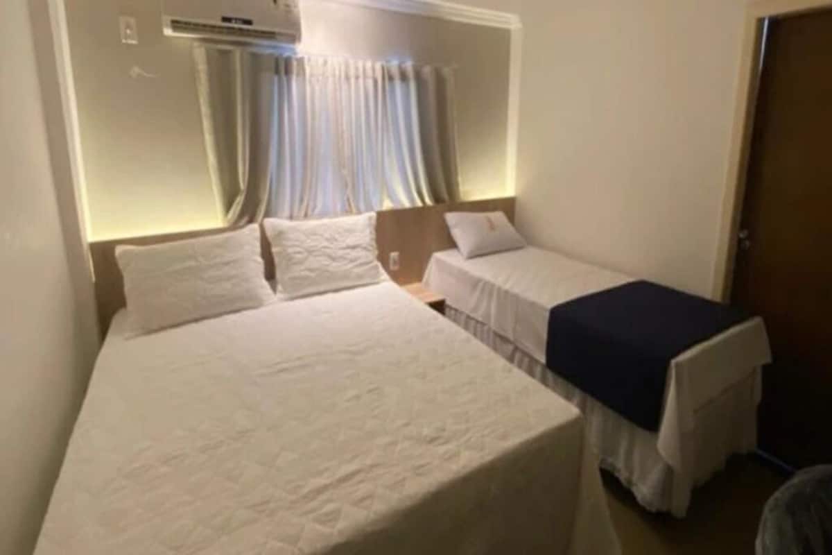 A hotel room with a large bed, a smaller bed, and a single bedside table.