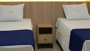 Deux lits simples avec des oreillers assortis, une petite table de chevet en bois avec un tiroir et une tête de lit en bois.