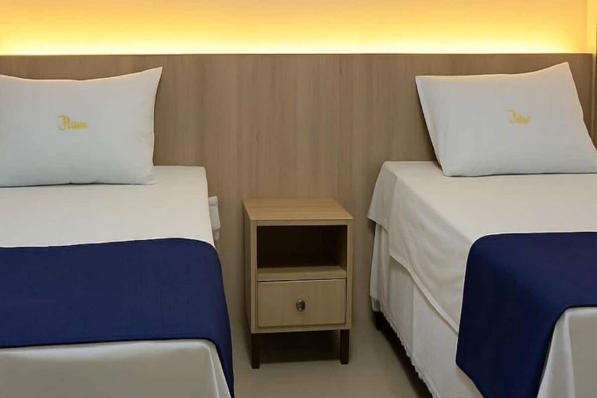 Two single beds with matching pillows, a small wooden nightstand with a drawer, and a wooden headboard.