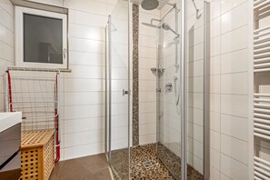 Eine Dusche mit Glastür, gefliesten Wänden und einem Fenster darüber.