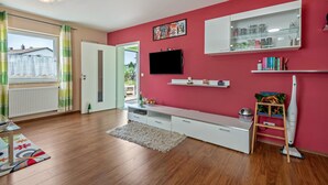 Un soggiorno moderno con pavimento in legno, un'unità porta TV bianca, TV a parete e una parete d'accento rossa.