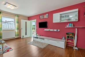 Una sala de estar moderna con piso de madera, un mueble blanco para entretenimiento, televisor montado y una pared de acento roja.