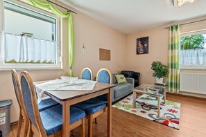 Ein Zimmer mit Esstisch, Stühlen, einer Couch, einem kleinen Couchtisch, einer Zimmerpflanze und einem Heizkörper.