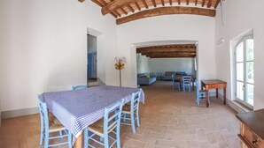 Una habitación amplia con una mesa a cuadros, sillas azules, un banco de madera y piso de piedra.