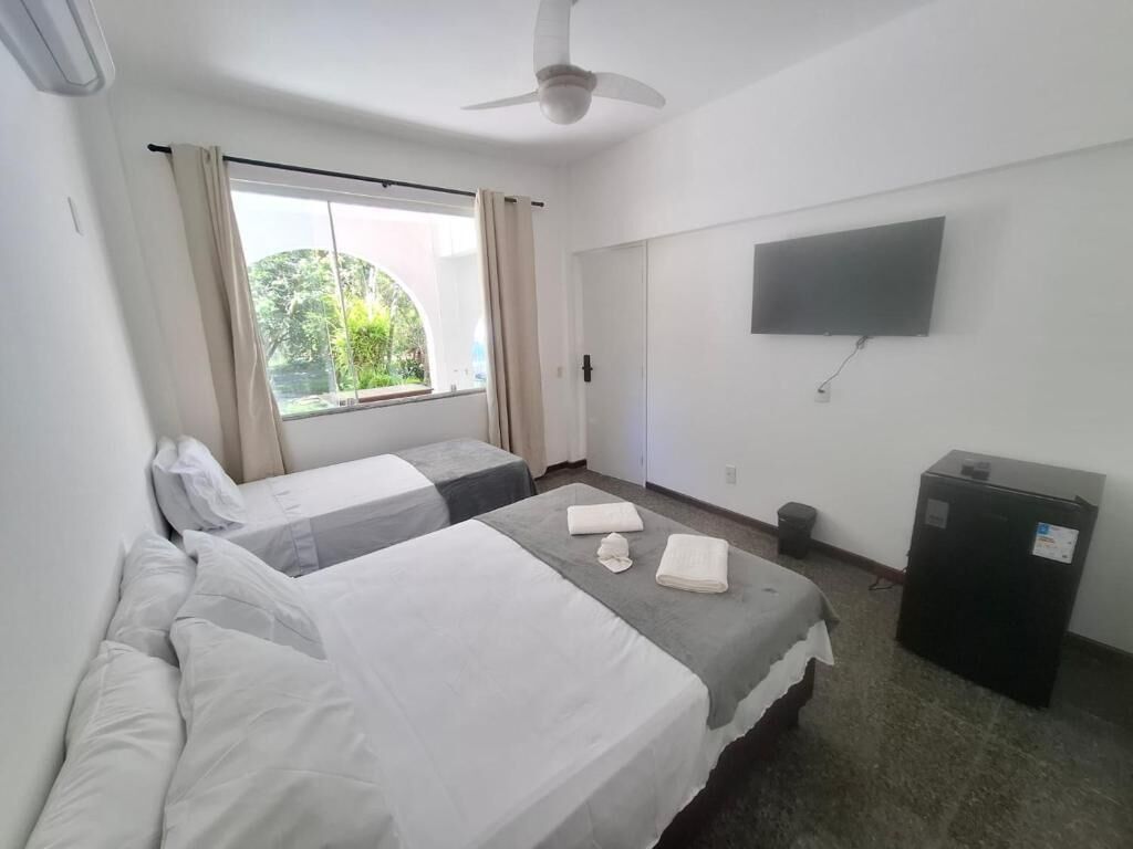 A hotel room with two beds, a ceiling fan, a TV, and a window with curtains.