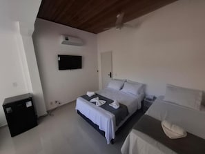 Ein Schlafzimmer mit Bett, einem Flachbildfernseher an der Wand, einem Deckenventilator und einem kleinen schwarzen Schrank.