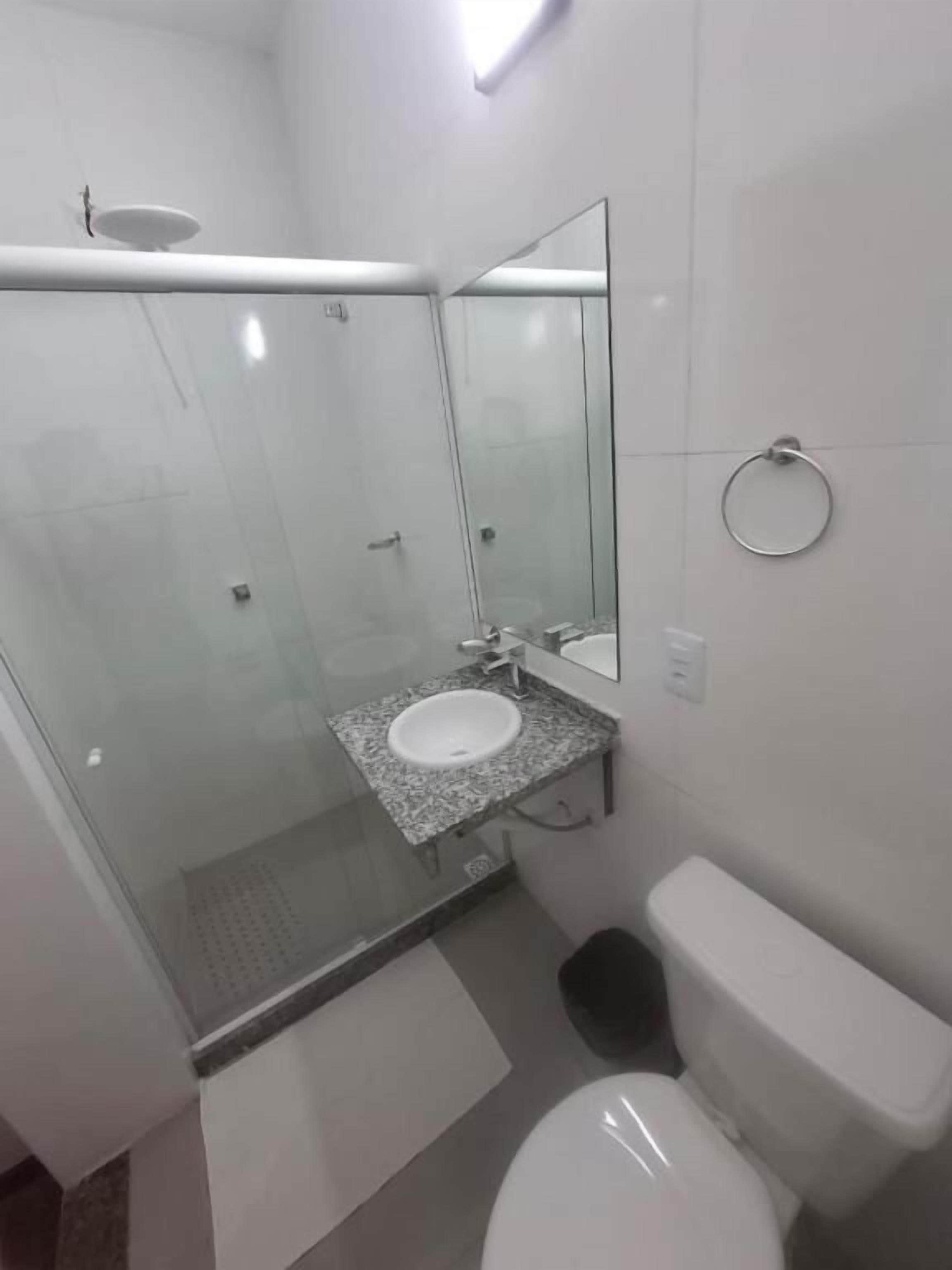 Um banheiro com chuveiro em gabinete de vidro, pia com bancada de granito, vaso sanitário e espelho.