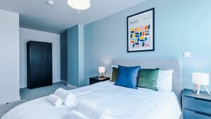 Une chambre d’hôtel moderne avec un grand lit, une armoire, une table de chevet avec une lampe et une œuvre d’art abstraite encadrée accrochée au mur.