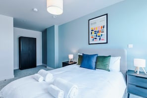 Ein modernes Hotelzimmer mit einem großen Bett, einem Kleiderschrank, einem Nachttisch mit Lampe und einem gerahmten abstrakten Kunstwerk an der Wand.