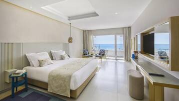 Une chambre d’hôtel comprenant un lit, un bureau, une chaise, une télévision et un balcon avec vue sur la mer.