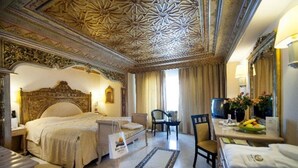 A hotel room with a large bed, a desk, a chair, a television, and a dining table with a vase of flowers. - Royal Azur Thalasso Golf (Hammamet)