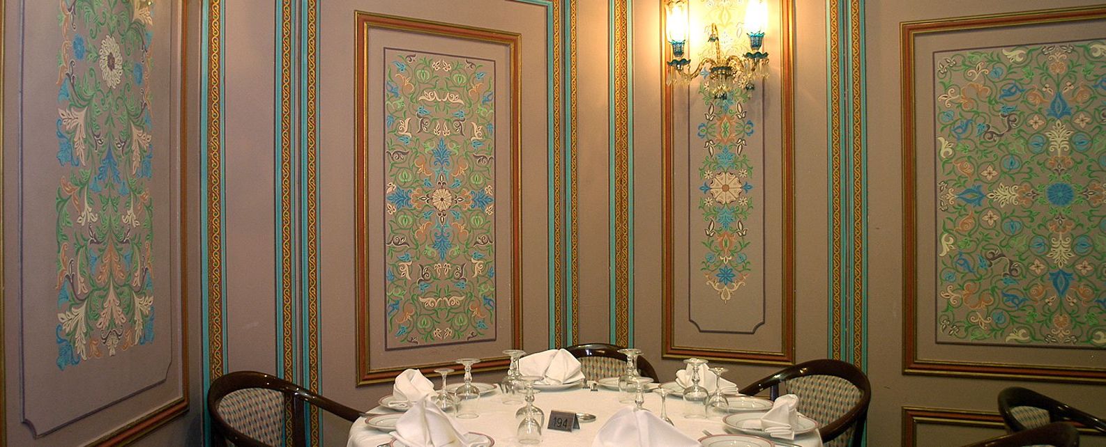 Une salle à manger avec une table ronde dressée pour le repas, des œuvres d’art encadrées aux murs et un lustre.