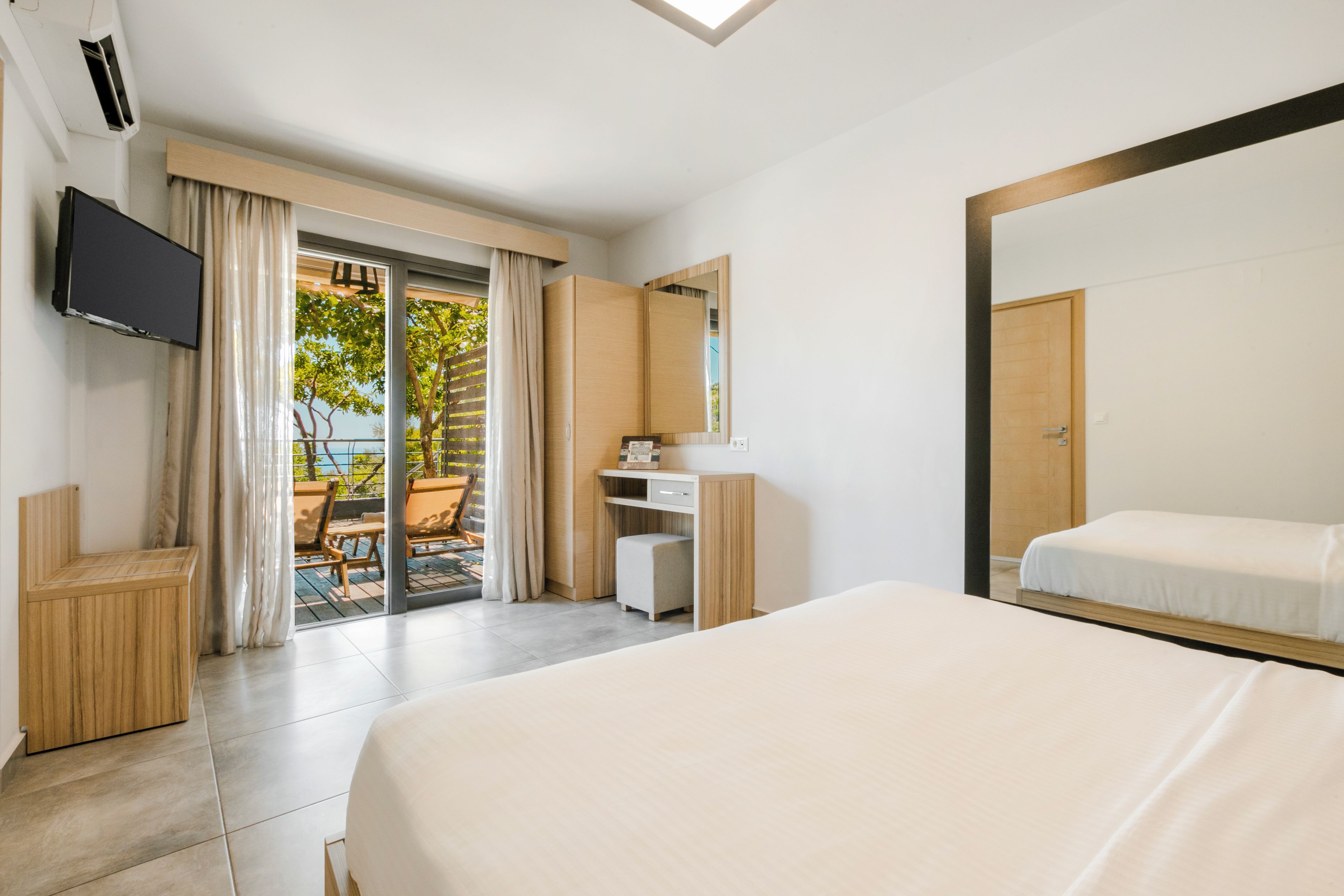 A hotel room with a bed, a TV, a desk, a chair, a mirror, and a sliding glass door leading to an outdoor area.