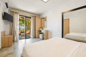 Habitación de hotel con cama, televisor, escritorio, silla, espejo y puerta corrediza de vidrio que da a un espacio exterior.