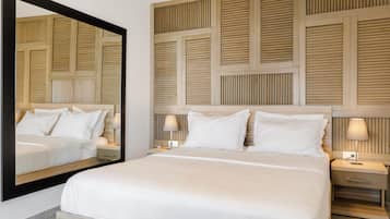 Un dormitorio ordenado con un espejo grande, una cama con ropa de cama blanca, dos mesitas de noche con lámparas y un cabecero de madera con diseño de listones.