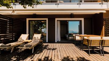 A wooden deck with lounge chairs and a table, a balcony with a railing, and a view of the sea.