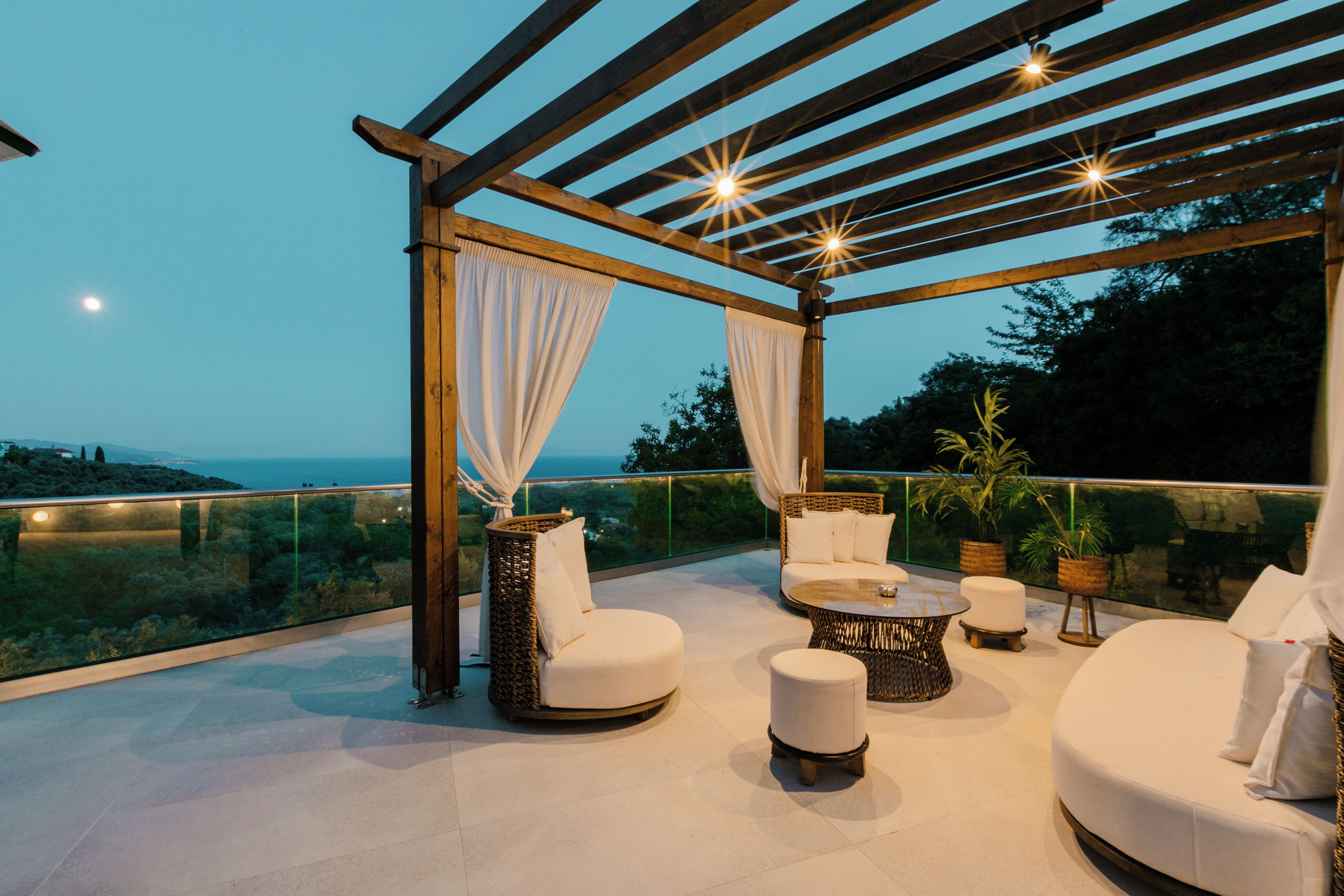 A covered outdoor seating area with wicker furniture, a round coffee table, and a view of the sea.