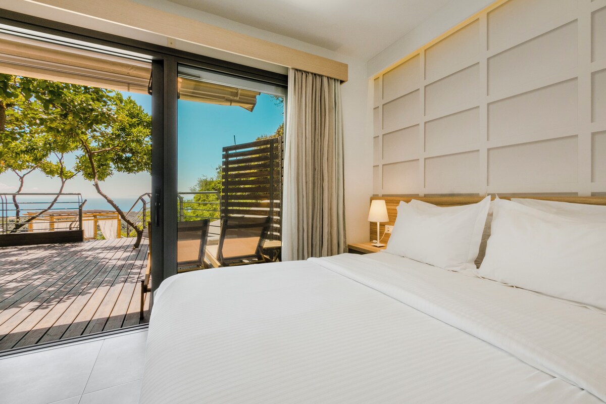 A hotel room with a large bed, a view of the outdoors, a balcony, and a wooden deck.