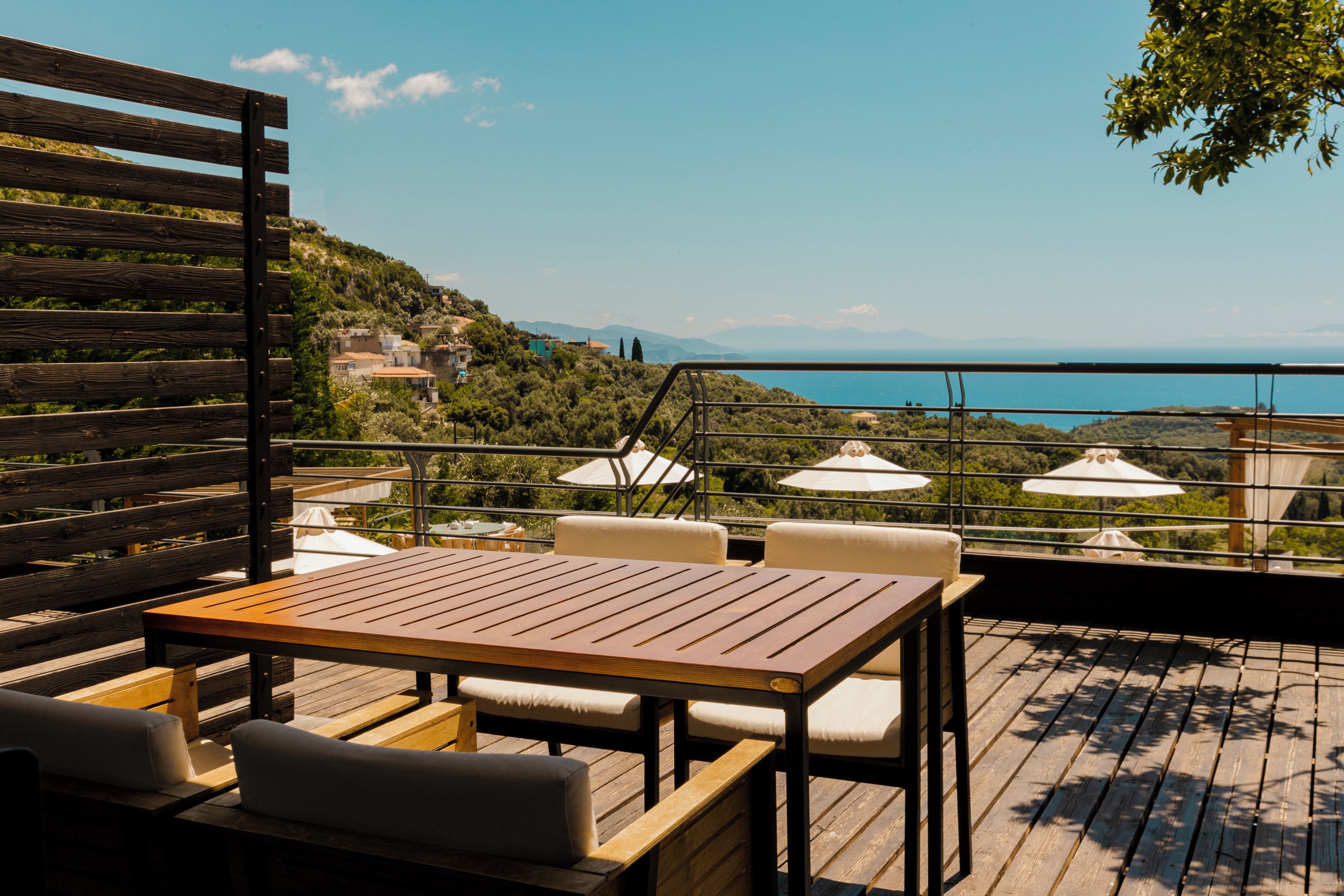 A wooden deck with a table and chairs, overlooking a scenic view of a body of water and hills.