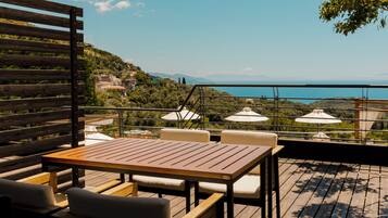 A wooden deck with a table and chairs, overlooking a scenic view of a body of water and hills.