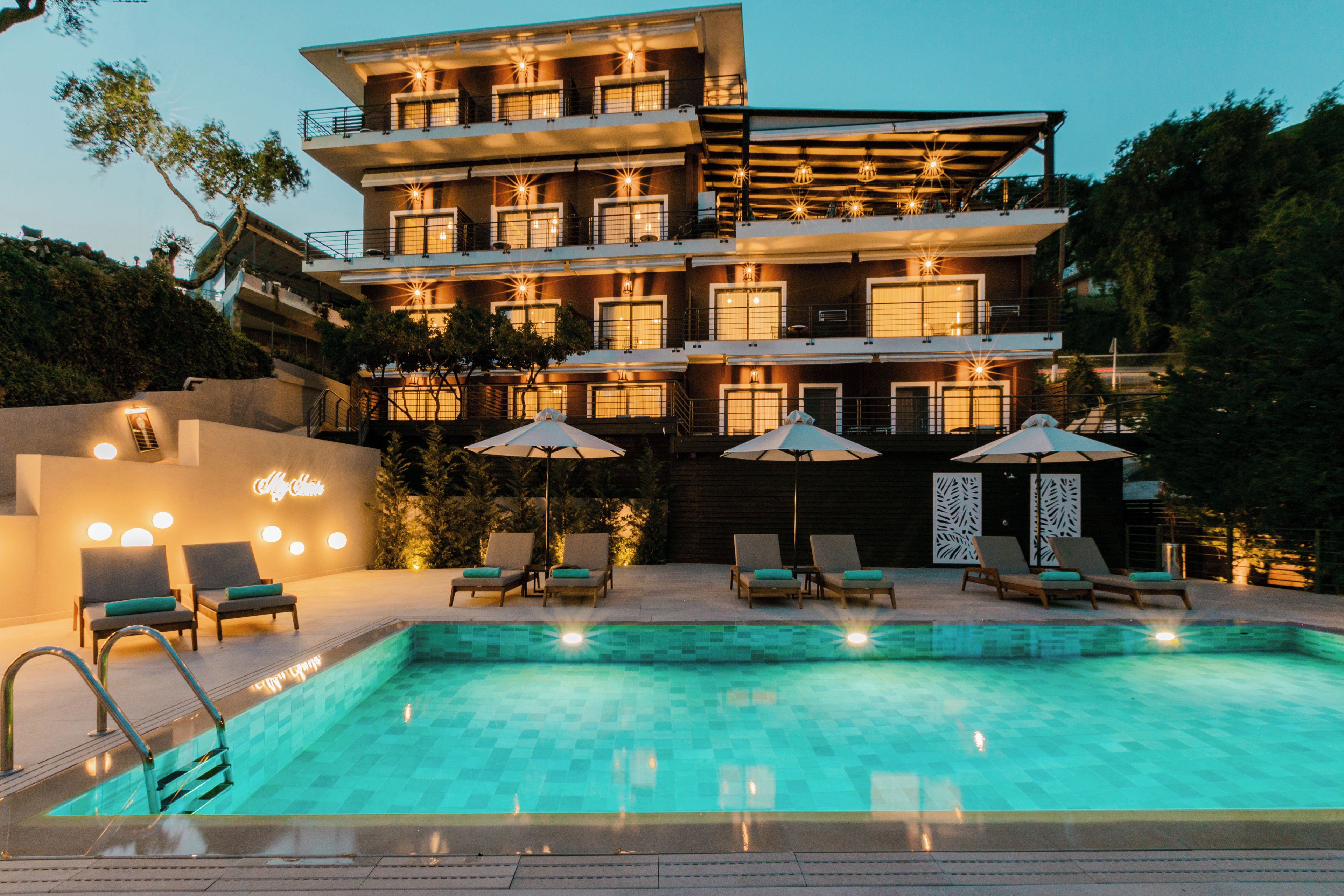 A multi-story hotel with a swimming pool, outdoor seating, and a well-lit facade.