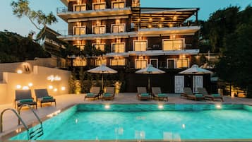 A multi-story hotel with a swimming pool, outdoor seating, and a well-lit facade.