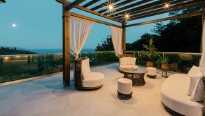 A covered outdoor seating area with wicker furniture, a round coffee table, and a view of the sea. - My Suite Boutique Hotel (Parga)