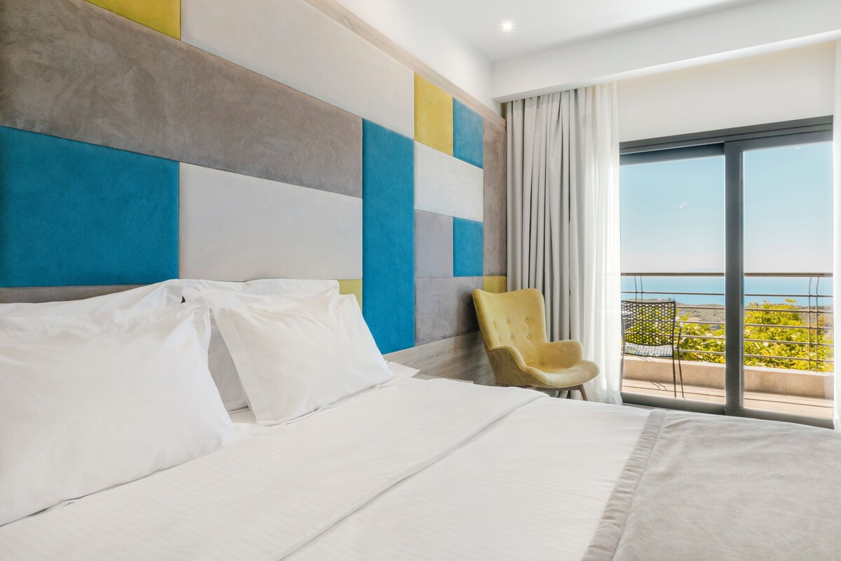 A hotel room with a large bed, a chair, a view of the outdoors, and a modern wall design.
