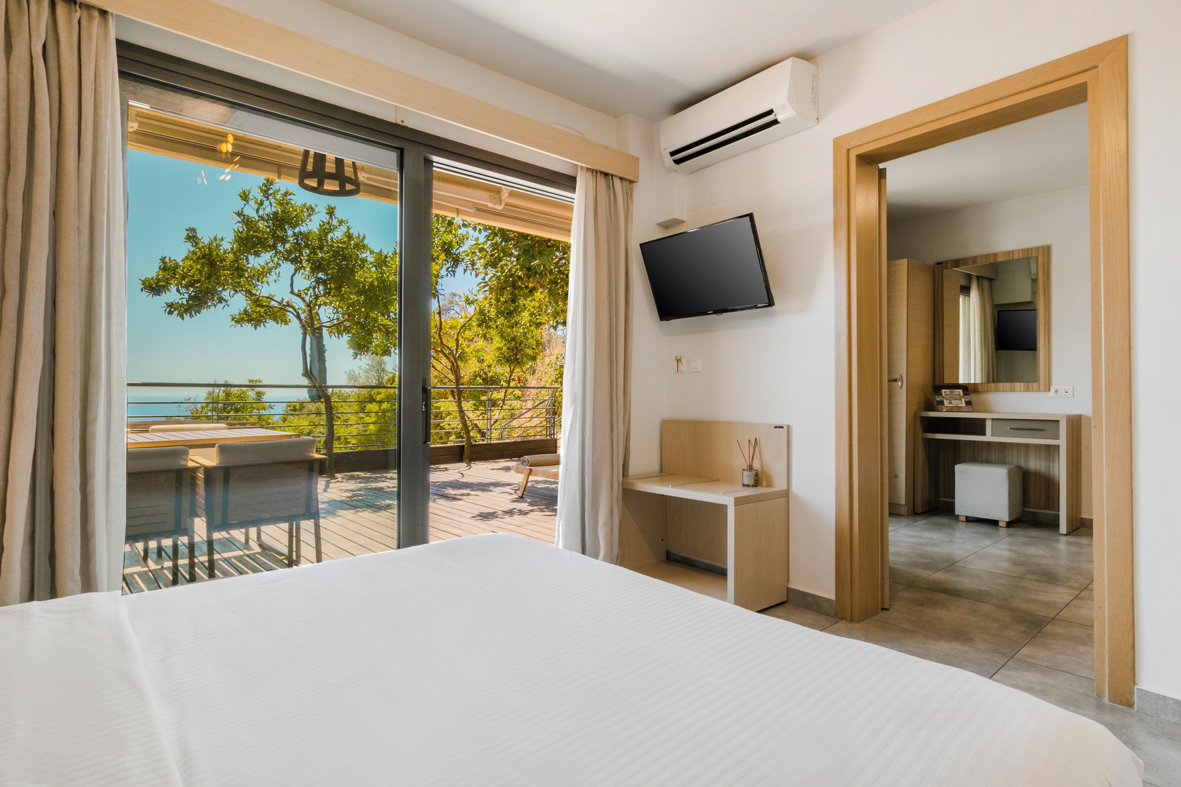 Ein Hotelzimmer mit Bett, Schreibtisch, Fernseher und einem Balkon mit Meerblick.