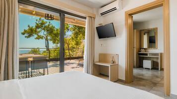 Ein Hotelzimmer mit Bett, Schreibtisch, Fernseher und einem Balkon mit Meerblick.
