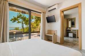 Quarto de hotel com cama, escrivaninha, televisão e varanda com vista para o mar.