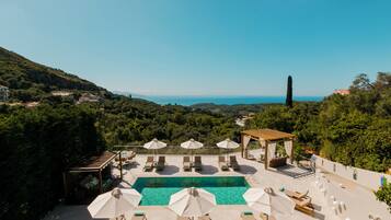 A rooftop pool area with lounge chairs, umbrellas, and a view of the sea.