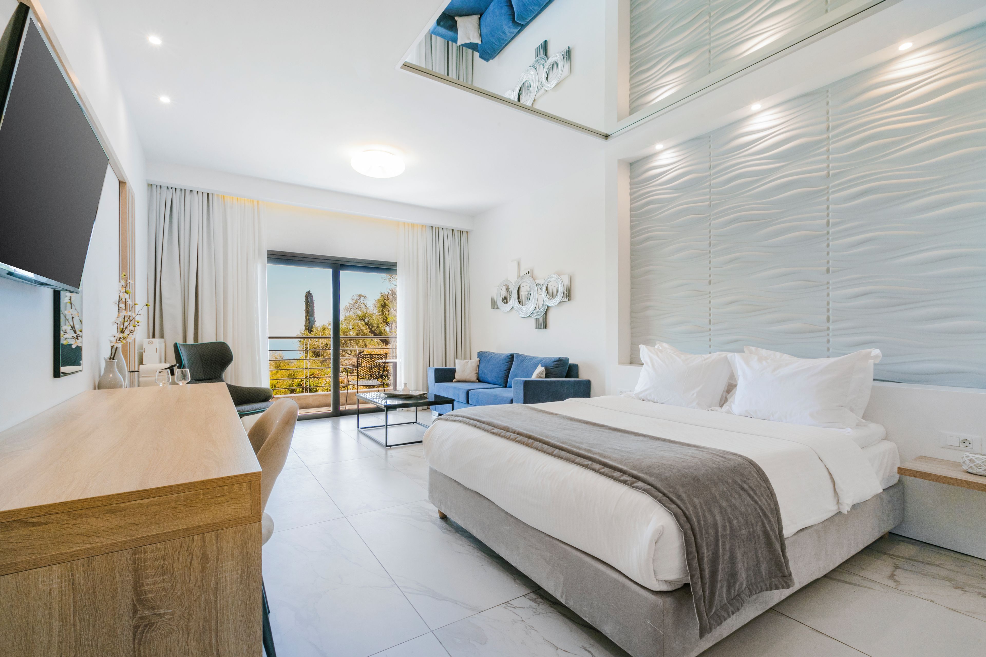 Ein modernes Hotelzimmer mit einem großen Bett, einem Schreibtisch, einer Sitzecke und einem Balkon mit Blick.