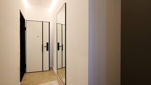 Un corridoio con una porta armadio a specchio, un interruttore della luce e un pavimento in legno.