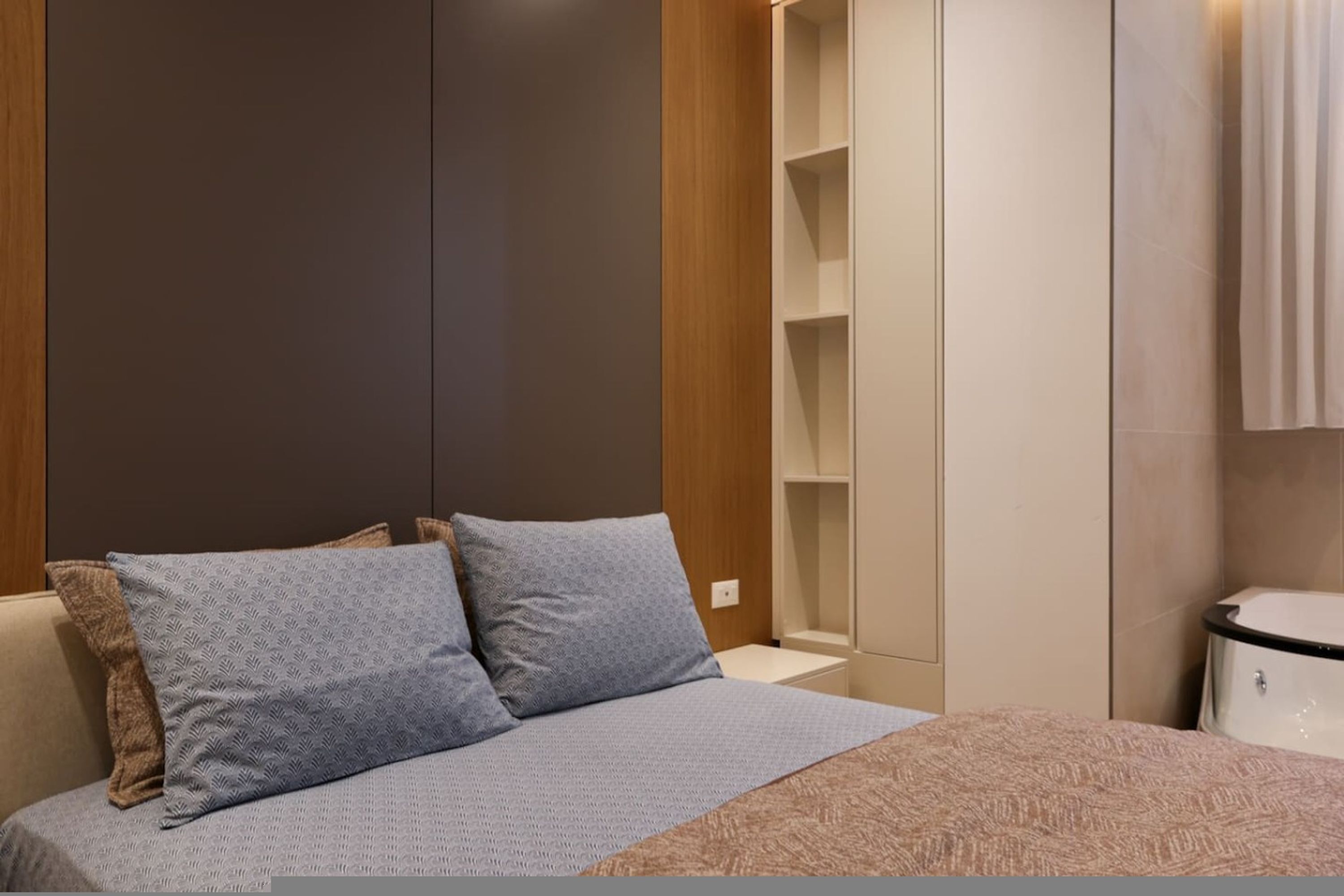 A bedroom with a bed, pillows, a nightstand, a wardrobe, and a bathroom with a toilet.