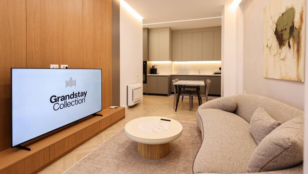 Un soggiorno moderno con una TV a schermo piatto, un tavolino rotondo, un divano e un'area cucina sullo sfondo.
