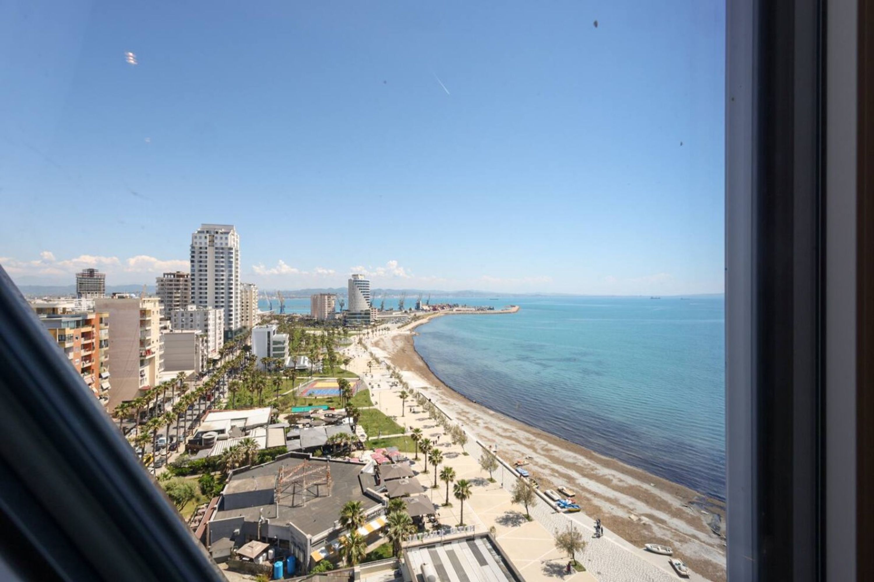 A coastal cityscape with high-rise buildings, a beach, and a clear sky.