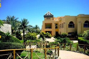 A hotel with a central tower, multiple windows, and a well-maintained garden with palm trees. - Rehana Royal Beach Resort (Sharm El Sheikh)
