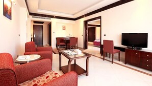 A modern living room with red upholstered sofas, a glass coffee table, a flat-screen TV, and a dining area with a small table and chairs. - Rehana Royal Beach Resort (Sharm El Sheikh)