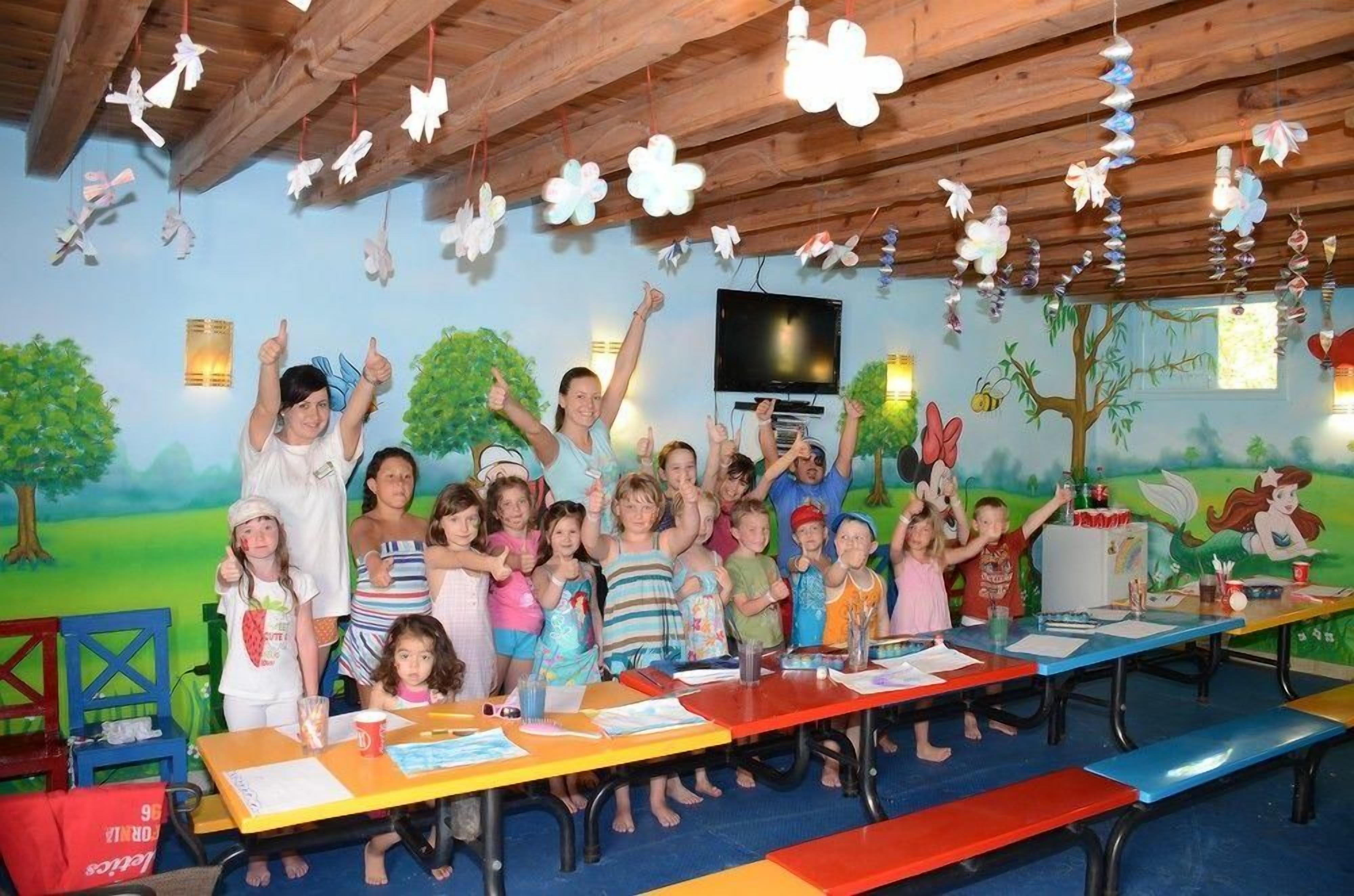 Un gruppo di bambini e adulti in una stanza con travi in legno, un murale e tavoli su cui sono sparsi fogli e materiali per l'arte.