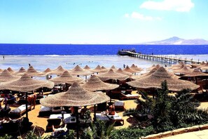 A beach with thatched umbrellas and lounge chairs, a pier extending into the water, and a mountain in the background. - Rehana Royal Beach Resort (Sharm El Sheikh)