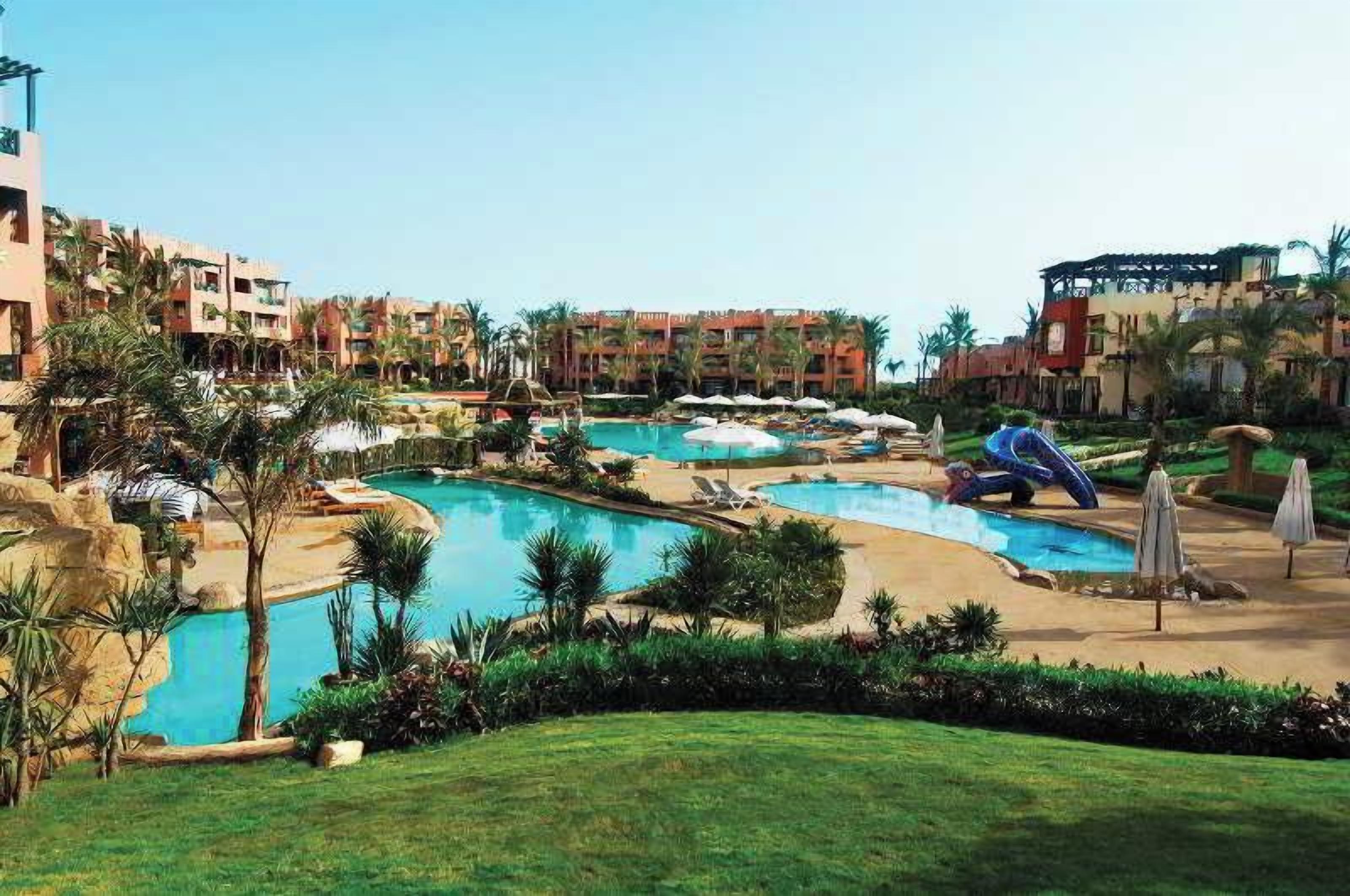 A resort with multiple swimming pools, palm trees, and a well-maintained lawn.