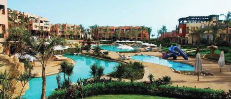A resort with multiple swimming pools, palm trees, and a well-maintained lawn.
