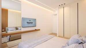 A modern bedroom with a bed, a TV displaying 'Grandstay Collection,' a wardrobe, and a built-in shelf. - Grandstay Sea Penthouse 02 (Durrës)