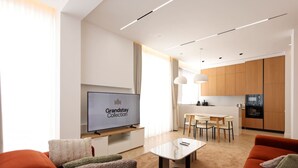A modern living room with a flat-screen TV, a dining area with a table and chairs, and a kitchen with wooden cabinets. - Grandstay Sea Penthouse 02 (Durrës)