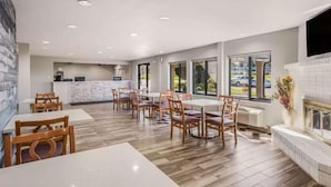 A spacious dining area with wooden tables and chairs, a kitchen in the background, and large windows. - Econo Lodge Inn & Suites Des Moines - Merle Hay Rd (Des Moines)