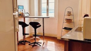 A small kitchen with a window, two bar stools, a hanging light, and a metal shelf. - Calvi plage T3 (Calvi)