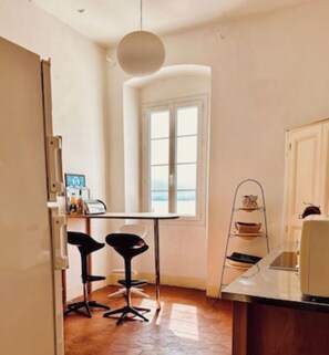 A small kitchen with a window, two bar stools, a hanging light, and a metal shelf. - Calvi plage T3 (Calvi)